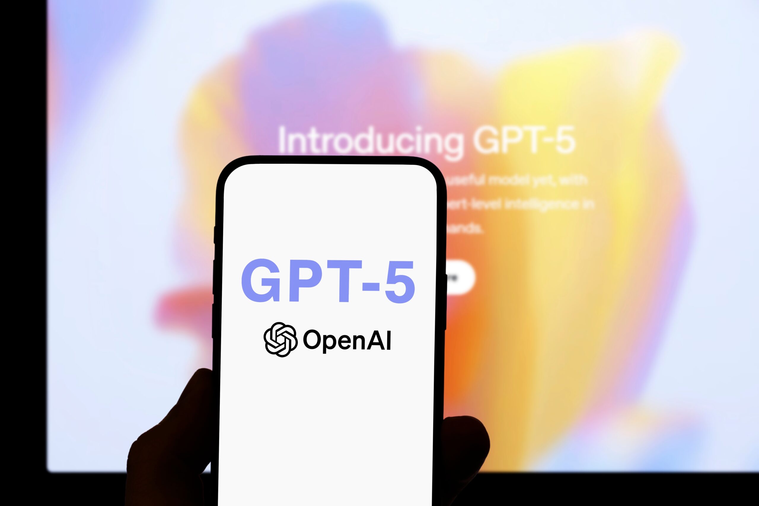 Smartphone showing GPT-5 OpenAI logo in front of a blurred screen with 'Introducing GPT-5' text, symbolizing ChatGPT 5 release, AI news, ChatGPT update, and AI for education advancements.